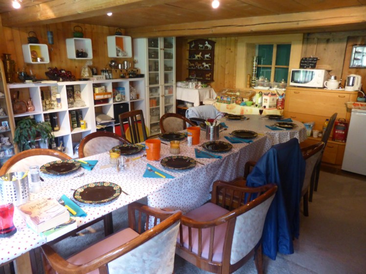 The dining room, a large room with a low wooden ceiling and wood-panelled walls, dominated by a long table, set with pretty plates. There's a microwave and a breakfast buffet table laid out at the other end and shelves full of interesting knick-knacks everywhere.