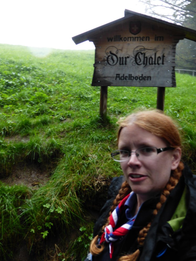 A selfie at the sign at the entrance to Our Chalet. The sign is huge and it has a sloping chalet-style roof over it. It's not the best picture of me though.