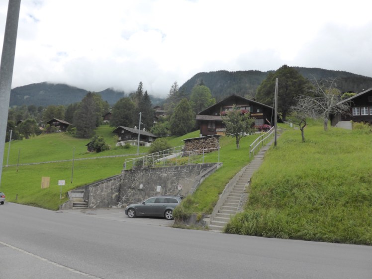 A small hill rising up from the road with a few chalets dotted on it and an almost invisible light rail line running about halfway up it. Our chalet is the on towards the left, not facing the camera, directly above the corner of the concrete car parking bay.