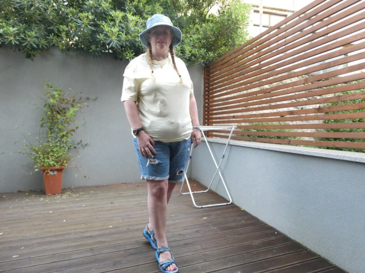Doing the crossed feet tiptoes pose, wearing a light yellow t-shirt with my denim shorts and sandals and a denim bucket hat.