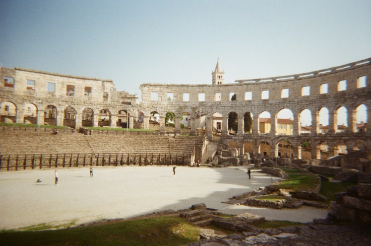 Inside Pula Arena, standing on a block on the west side, looking across to the surviving tiered seating on the west side of the ring.