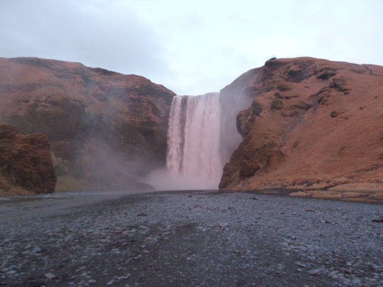 Skogafoss, a waterfall around 60m wide and high slightly pink-tinted by the sunset.