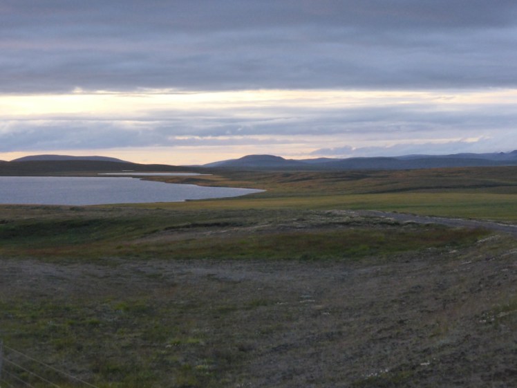 A lake in the north of Iceland at 10pm on July 31st 2016. Although there's quite a thick layer of clouds, you can see the sky behind and it's the pale pink/pale yellow of early sunset.