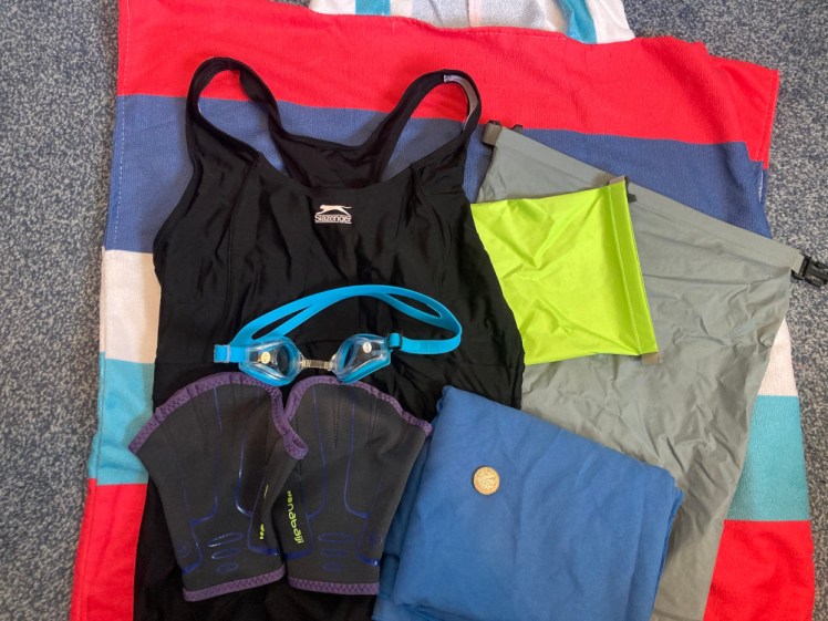 My swimming stuff - a stripey towel-robe with a small drybag, a travel towel, a black swimsuit, a pair of neoprene training gloves and a pair of prescription goggles.