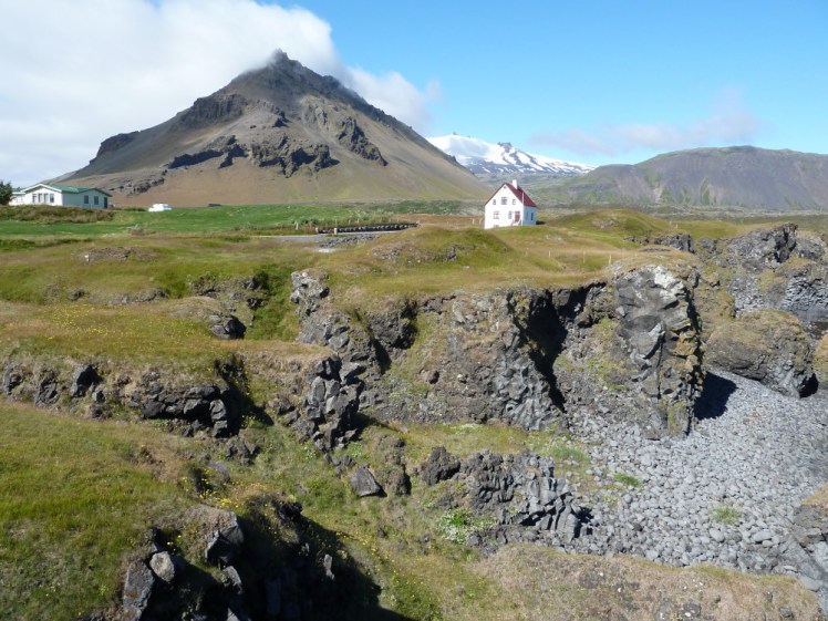 Arnarstapi, a small village with a little white house making the focal point for two mountains behind it, one a grey-brown dusty pyramid and one a snow-covered volcano.