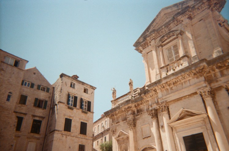 Blue sky over yellow-white stone buildings. The big one to the right is Dubrovnik's Baroque-style cathedral.