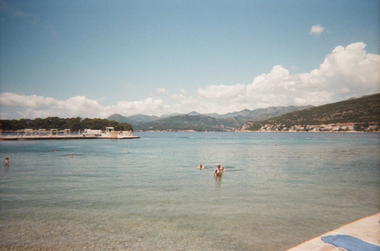 A very blue, even on 35mm film, bay with a low harbour wall enclosing the far side and the port part of Dubrovnik across the water.