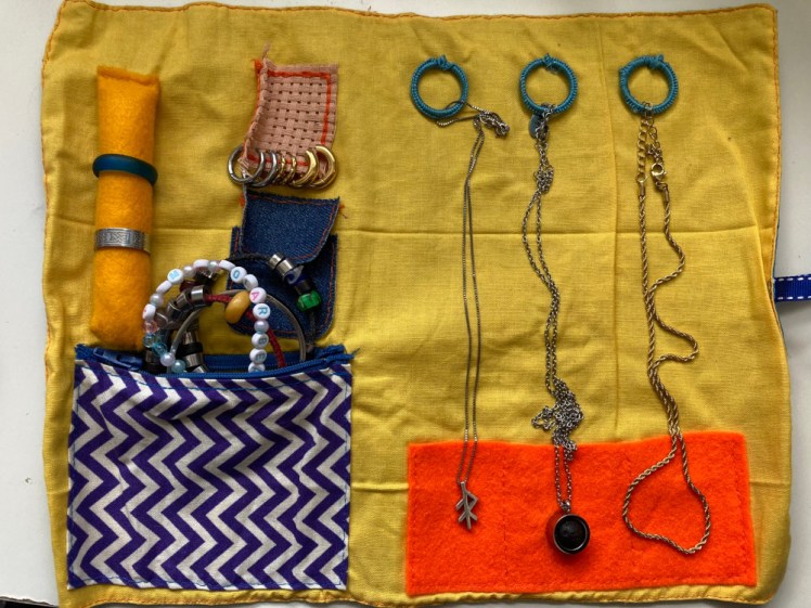 My jewellery roll, a yellow piece of fabric backed with blue, with rings and pockets to secure necklaces, a piece of aida for earrings, a tube for rings and a pocket for miscellanous bits, like the bracelets poking out.