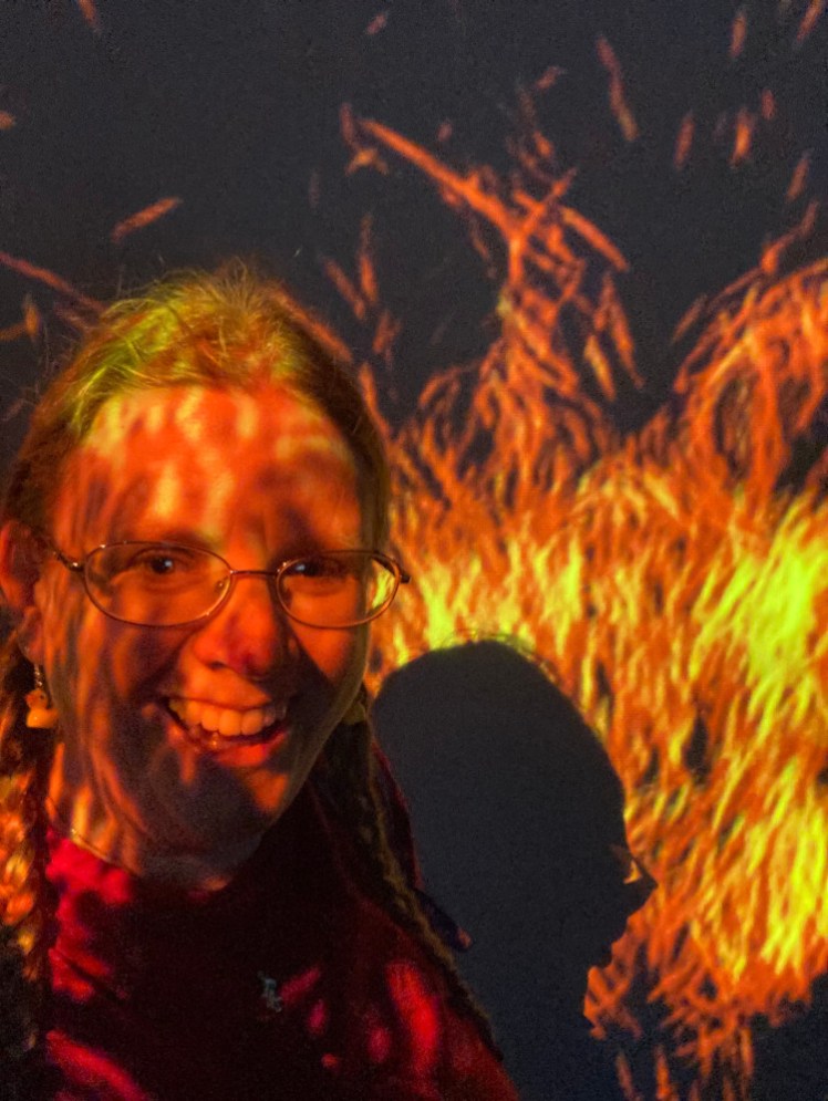 A selfie in the projected exhibition with flames across the wall and my face.