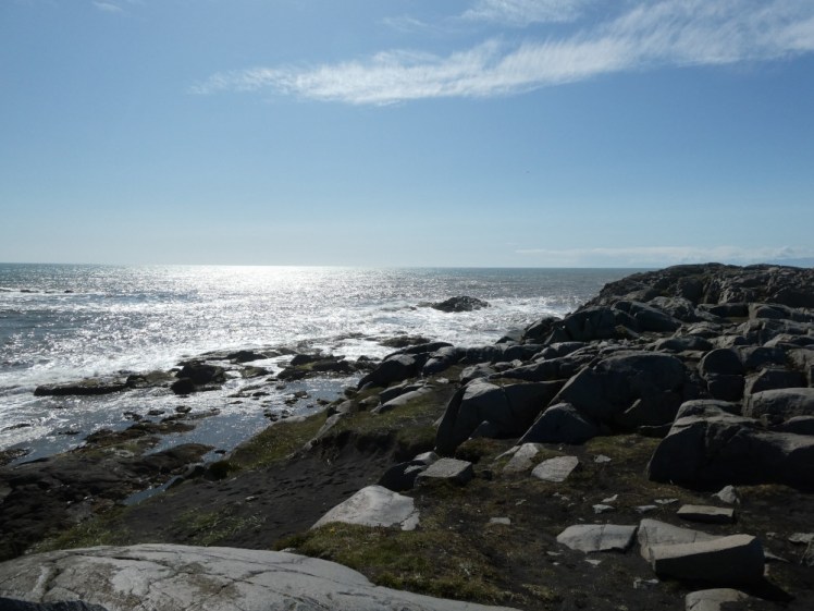 On the rocks, looking down at the sea crashing on the rocks below, while the sun shines on the water on the horizon.
