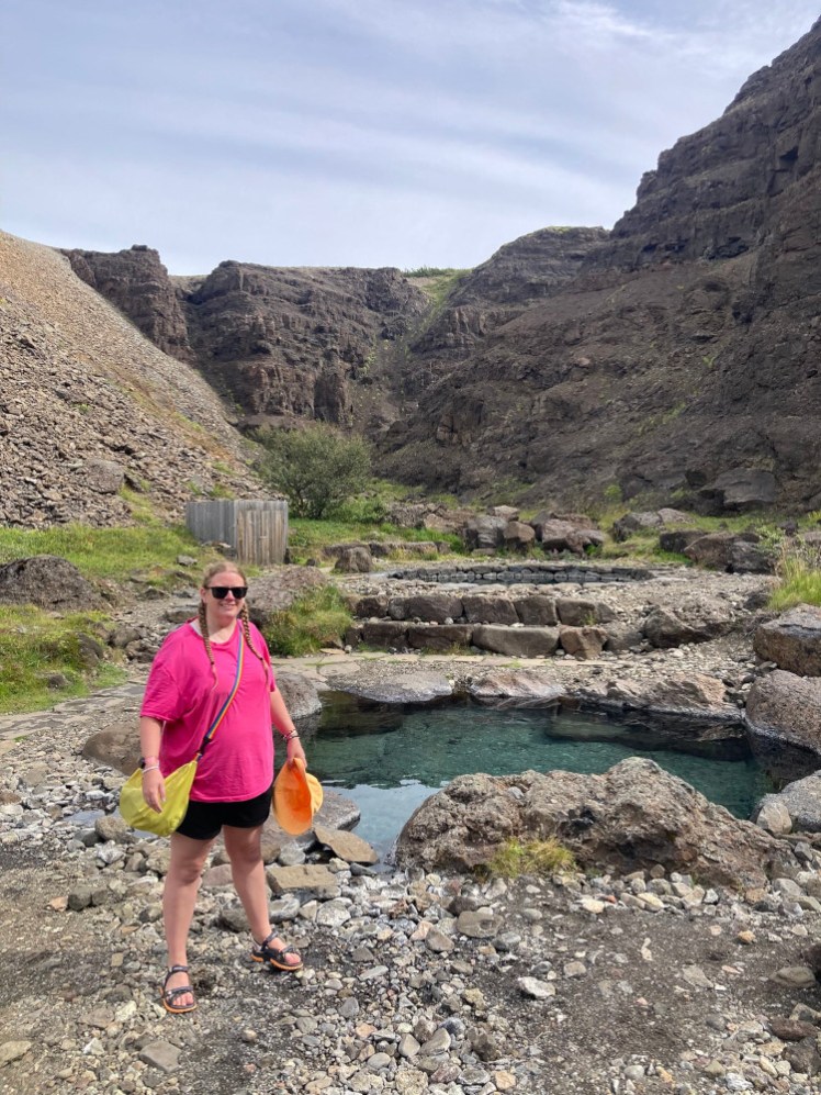 Me standing next to the two pools in the canyon, wearing a bright pink oversized t-shirt. There are two pools behind me in a steep-sided canyon.