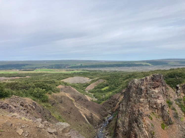 A view from the top of the canyon as it runs towards a flattish landscape with a mountain gently rolling upwards from it.