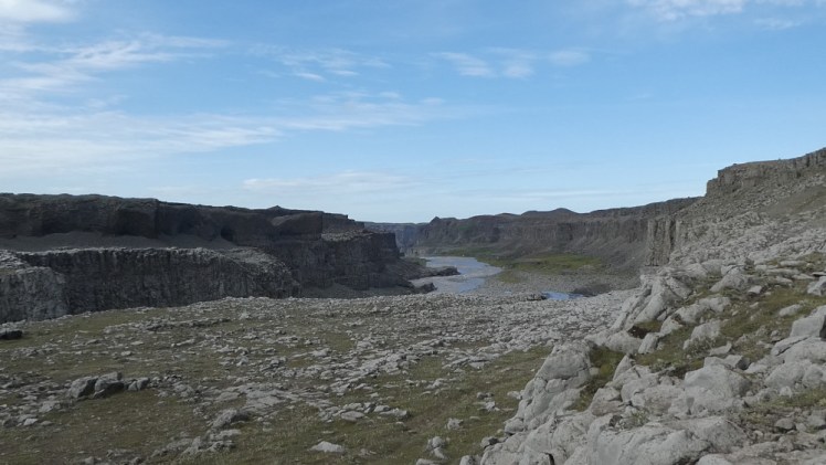 The river winding its way up a canyon much wider than the river itself. The steep walls are grey and the whole place is made of shattered rock but there's a lot of greenery around the edges and the sky overhead is blue. On overcast days, this whole scene is spectacularly grey in a post-apocalyptic way.