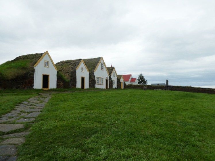 A row of turf houses at Glaumbær, houses built entirely out of wooden frames covered in turf with grassy sides and roofs and "fake" wooden fronts to give them the look of houses. The upstairs windows open onto nothing.