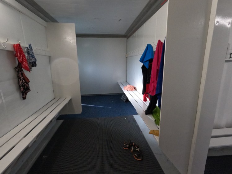 Inside the Grettislaug changing rooms, a very bare white room with a rubber mat on the floor, with wooden benches and pegs around the edges.