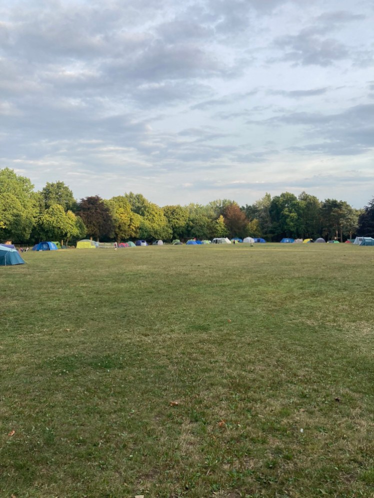 THe main camping field, which is a long field with trees around the edge. Down the far end are lots of tents, mostly arranged nicely around the perimeter of the field.