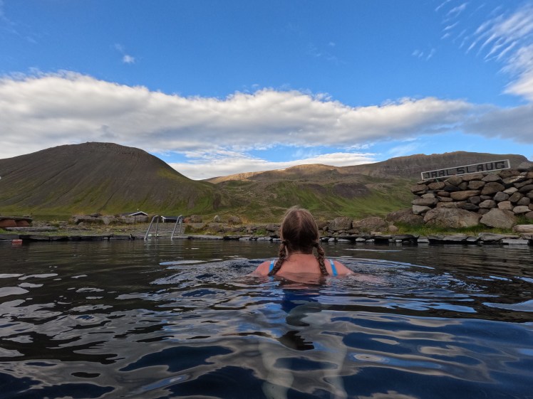 Me with my back to the camera looking at the mountains from the warmer pool early the next morning, with a vivid blue sky above me at last.