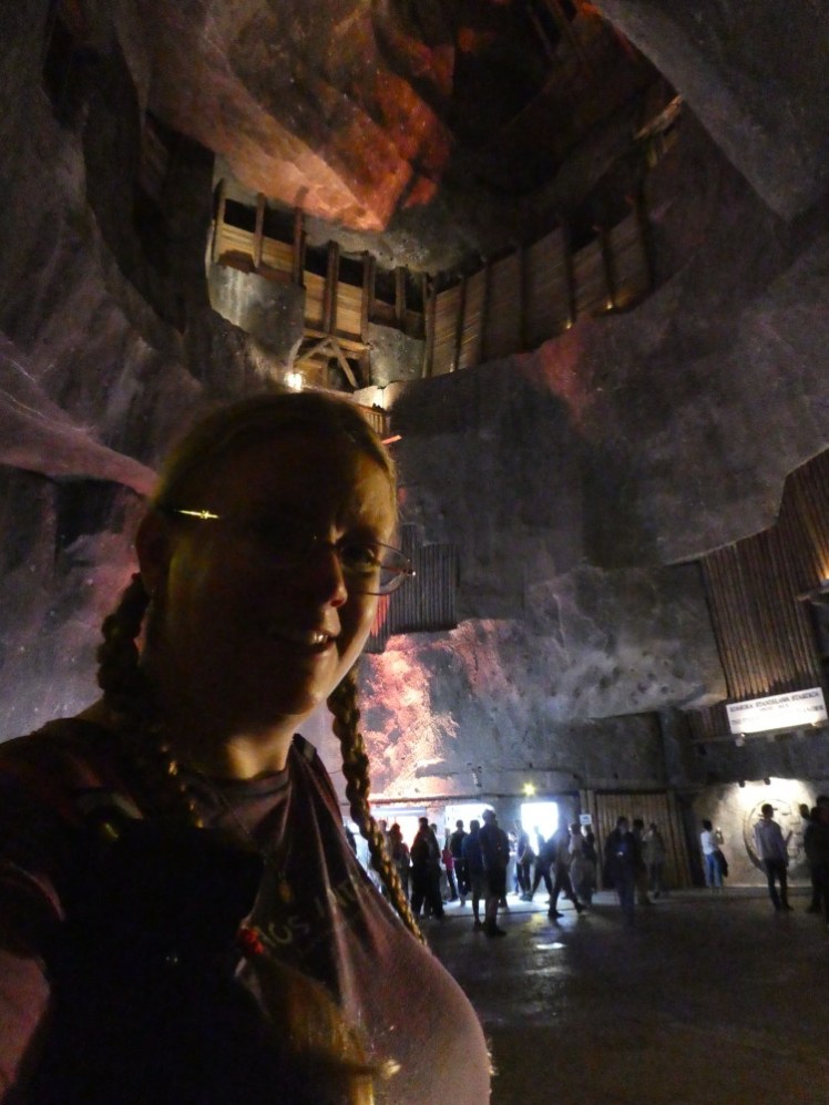 A selfie in a tall thin chamber where a kind of hole in the ceiling is lit in red while the lower levels are more purple.