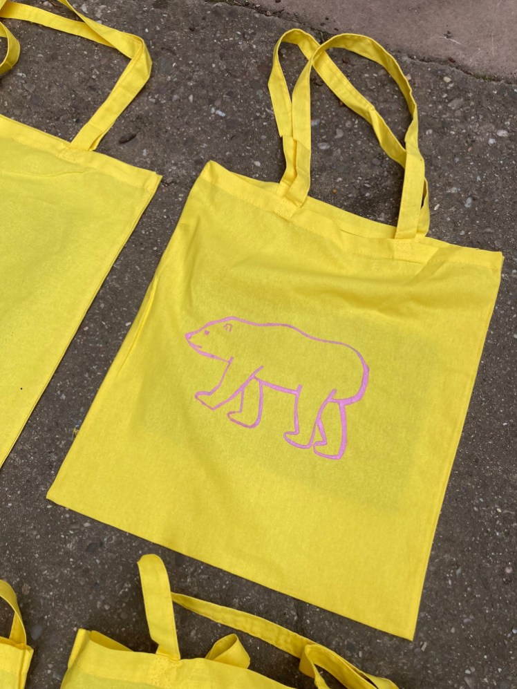My bag, lying in the sun to dry. It's a yellow cotton tote bag with the outline of a polar bear screenprinted onto it in pink.