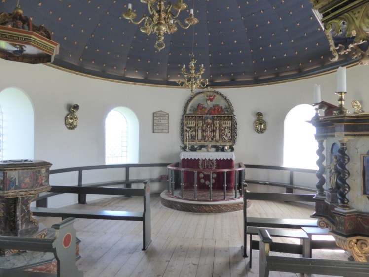 The inside of Þingeyraklausturskirkja, a small church with white walls and a blue ceiling dotted with a thousand gold stars. There's quite an elaborate lectern on one side and font the other and the altar is a lot more decorative than you might expect in a small church like this.