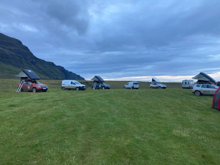 A collection of vans and cars with roof tents forming part of a circle around the edge of the field. Mine is the one parked nose i, fourth from left.