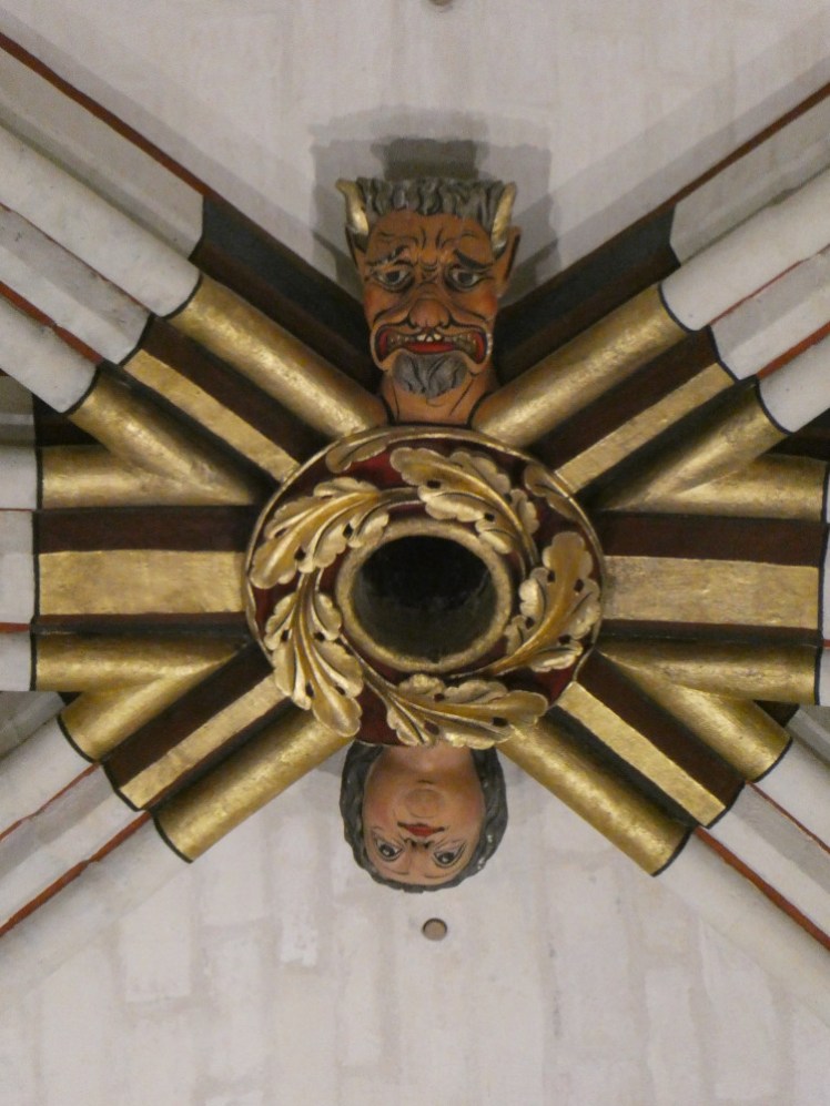 One of the ceiling bosses, a gold piece connecting six beams, with a crown of leaves in the middle, a horned head with a grey beard and gold horns on one side and a shocked lady on the other.