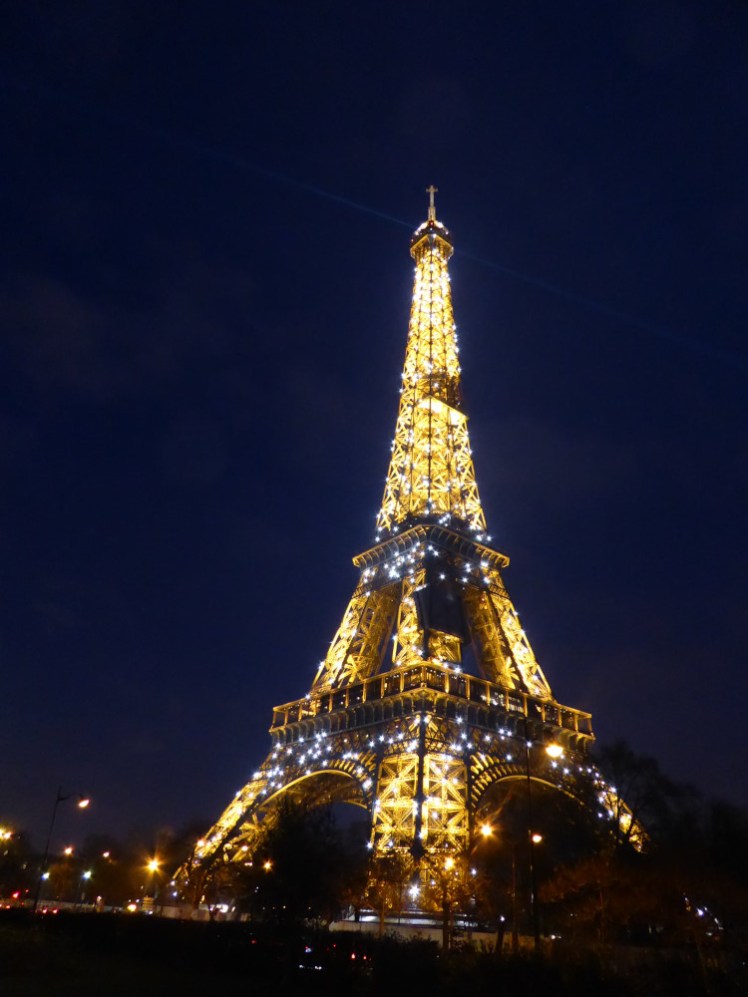The Eiffel Tower, illuminated in yellow with lots of cold-white lights sparkling all across it against the navy blue sky.
