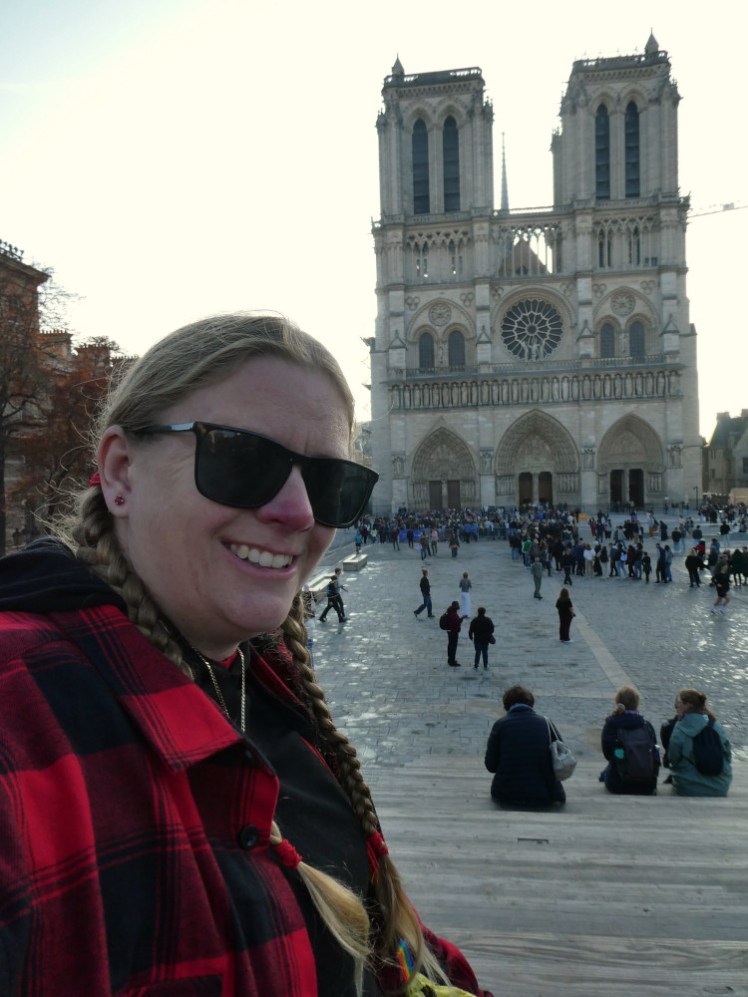 A selfie with Notre-Dame in the background sitting on the raised steps at the opposite end of the square.