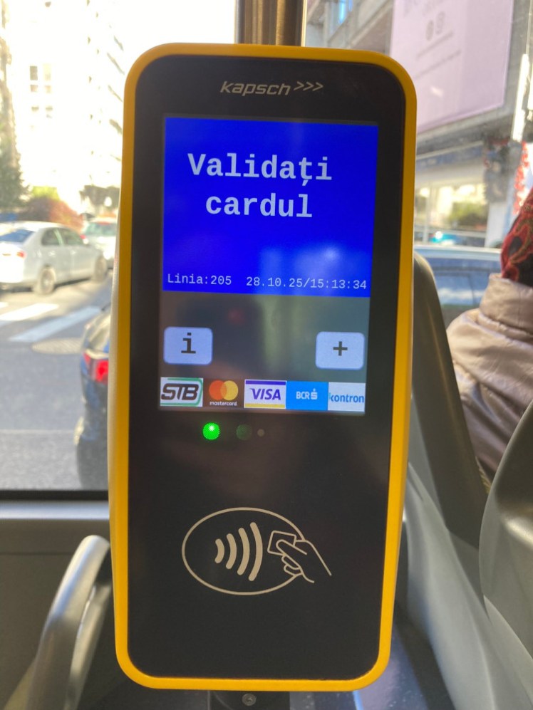 A validating machine on a bus. It's yellow with a bright blue screen asking you to "Validati cardul" and underneath is the contactless logo.