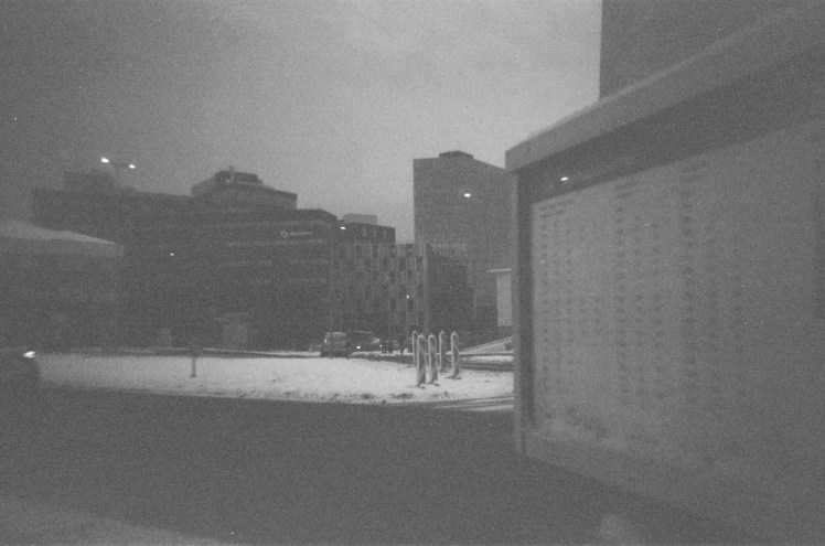 A close-up of a timetable on a bus stop in Reykjavik with relatively high-rise buildings (by Icelandic standards) behind it.