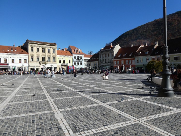 The Council Square in Brasov, with a cobbled floor and medieval-style buildings all around it.