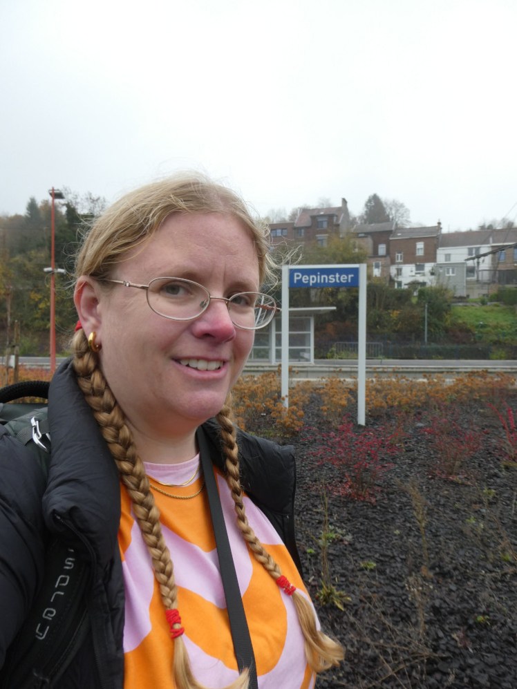 A selfie at Pepinster. Now I'm wearing a t-shirt in wavy pale pink and orange stripes under a black down jacket. It's a grey damp day but not actually raining.