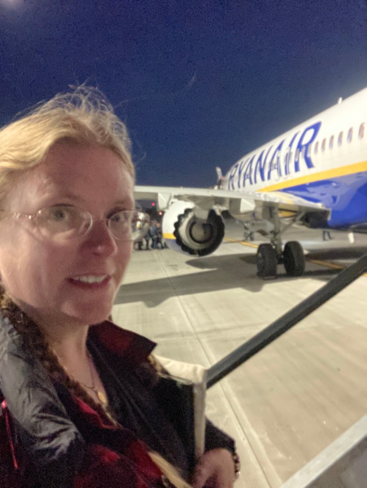 A selfie wearing all the clothes that wouldn't fit in my bag, outside in the dark with a Ryanair plane.