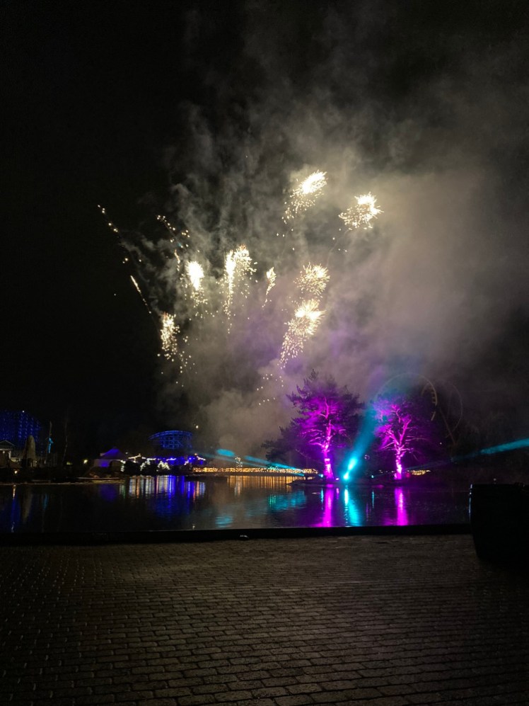 The firework finale over the lake, with blue and purple lights illuminating a small island, fireworks exploding above and Tonnerre 2 Zeus in blue in the background.
