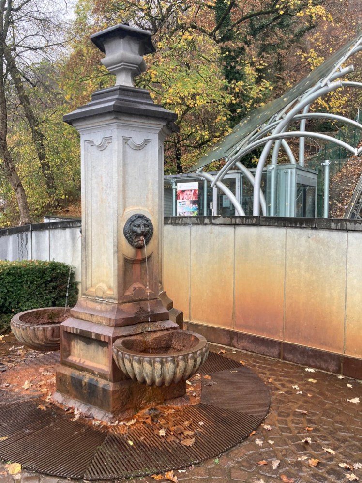 A fountain, now bright orange and with the wall behind it orange wherever the water has splashed. There are clearly a lot of minerals in the water. If you look in the bowls where the water pours from the tap, the minerals have eaten right through and it now pours straight into the drain.