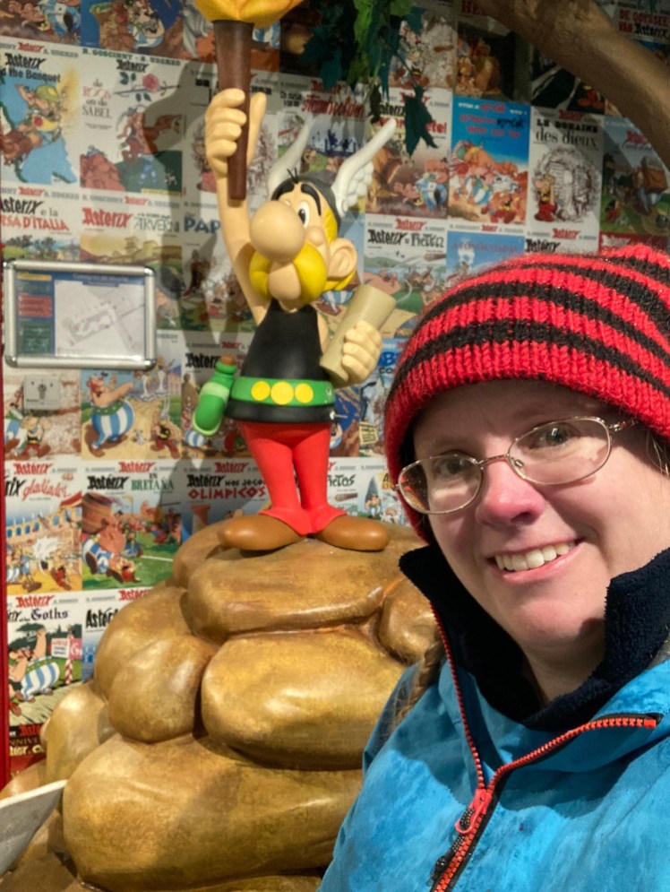 A selfie with a miniature Asterix statue and a background of Asterix comic panels.
