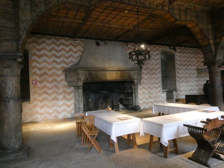 Aula Nova, a large medieval dining room where the walls are painted in (restored) off-orange and white chevrons, with a huge fireplace.