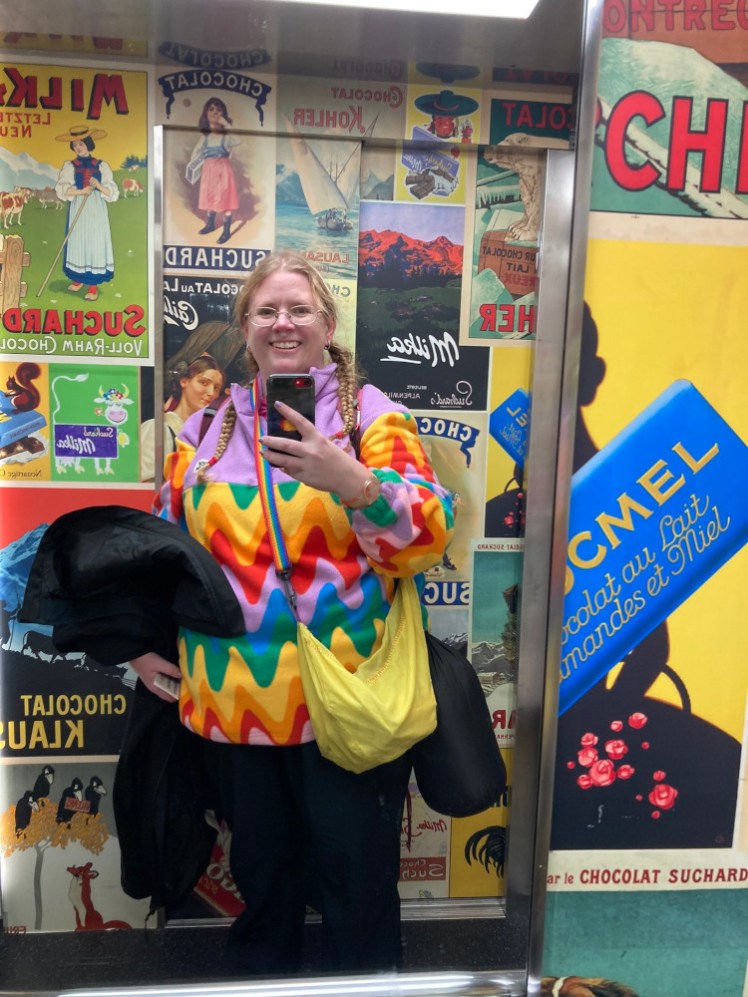 A mirror selfie in a lift plastered with vintage chocolate adverts. I'm adding to the colour by wearing a rainbow coloured fleece.