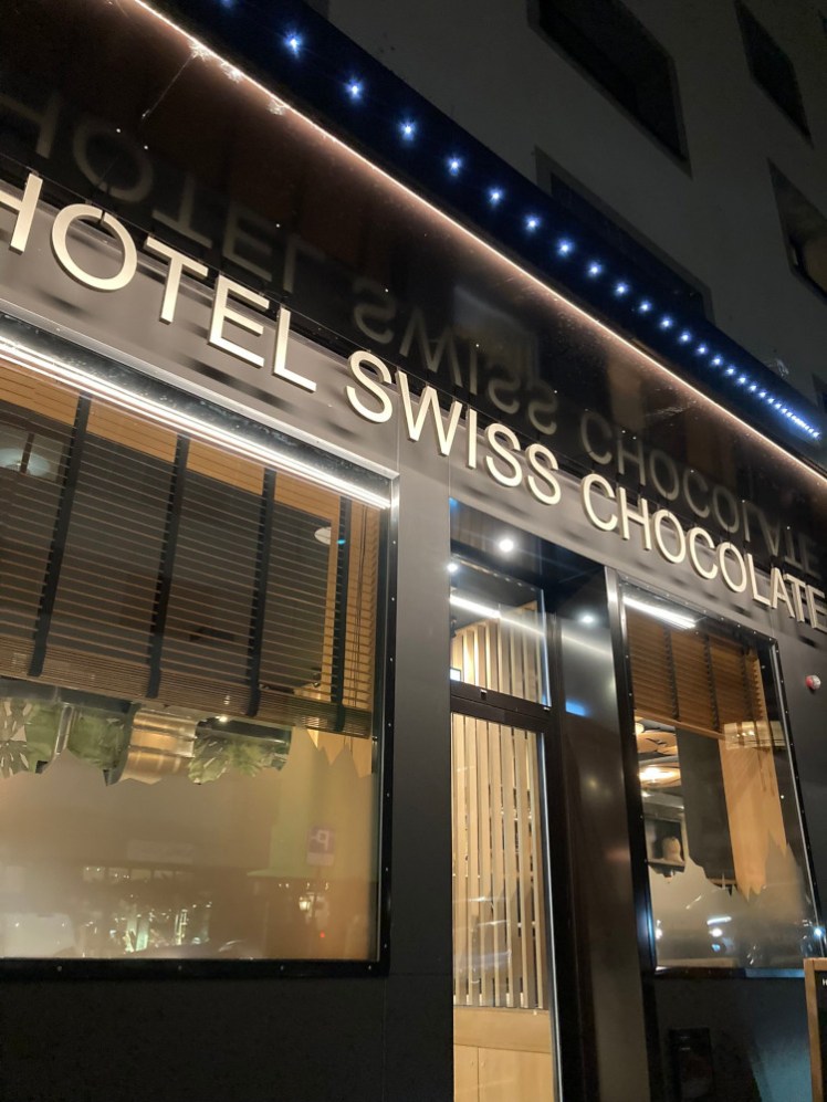 The outside of the Hotel Swiss Chocolate, which is just an ordinary brown hotel front with its name in cream-beige letters over the front.