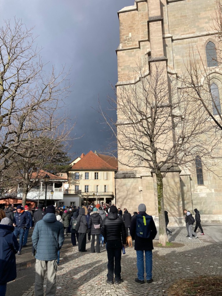 A crowd of people standing outside the west end of Lausanne Cathedral, waiting for the minute's silence to start. The sky above is dark in a way that suggests any second it's going to pour with rain, but it never happened, not at the cathedral.