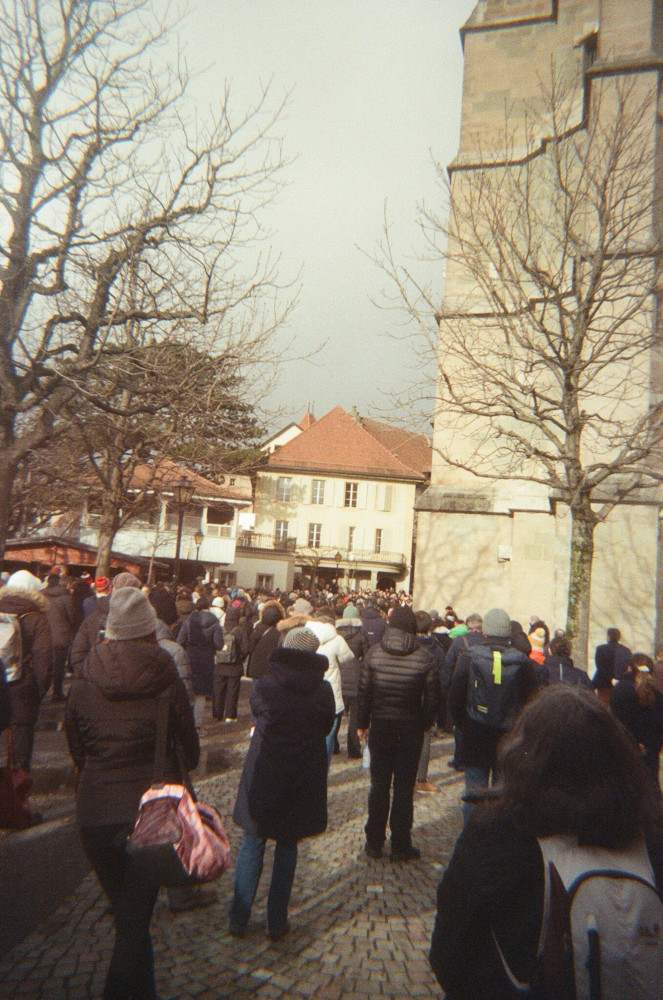 A crowd of people gathered in front of Lausanne's cathedral, which is surrounded by bare trees.