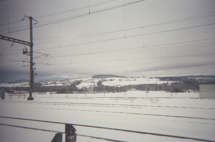 A field of snow and heavy snowy clouds as seen from a station - you can see the tracks and the lines between me and the view.