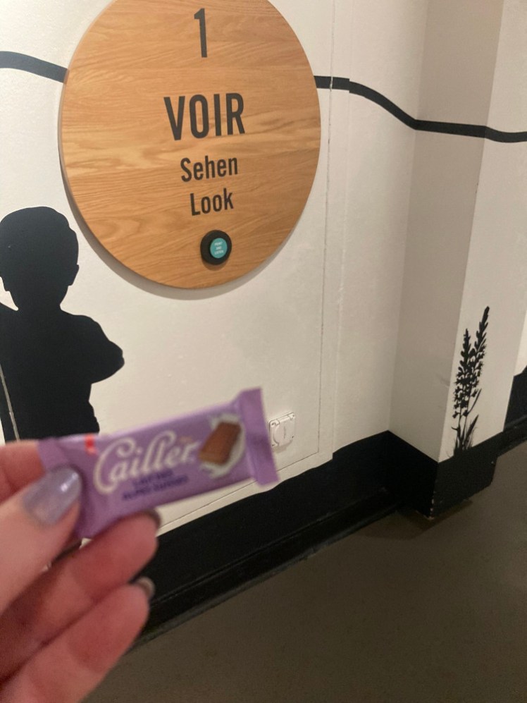 A tiny purple Cailler bar held up in front of tasting step 1, "Look".