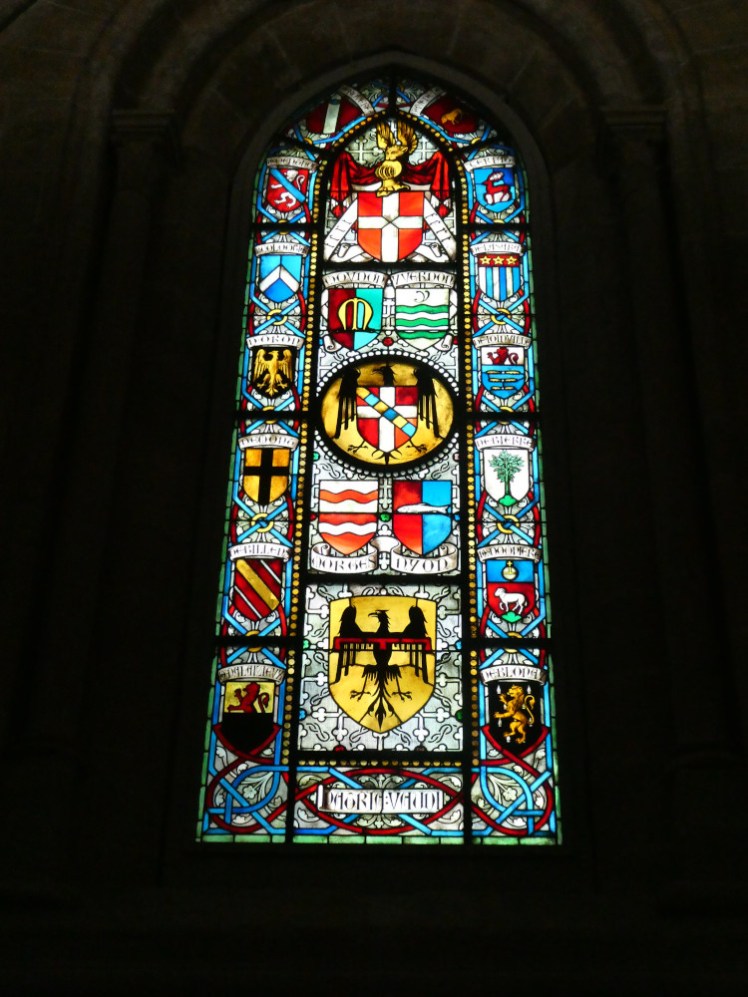 A window depicting local coats of arms. In the centre are Moudon, Yverdon, Nyon & Morges with smaller ones down the sides and headed by the Swiss flag.