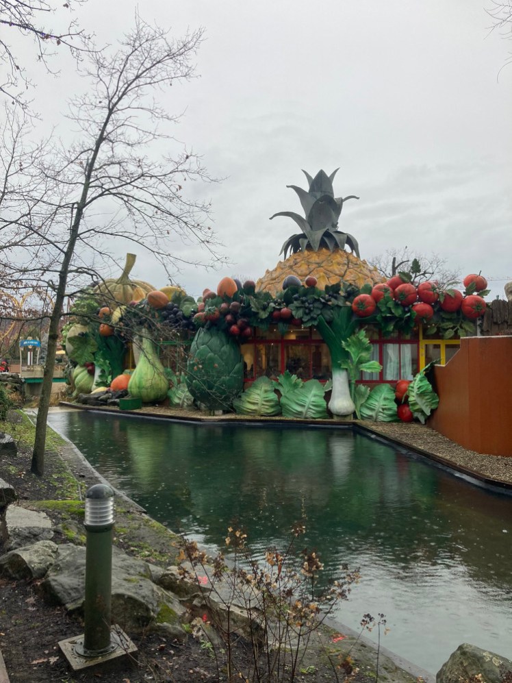 A restaurant on the edge of the lake, surrounded b a water ride. The restaurant is entirely decorated in giant fruit and vegetables.