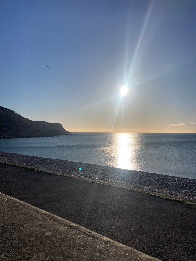 The view down the west cliff of Portland from the Cove Inn, with the sun getting low over the sea and a hint of orange on the horizon.