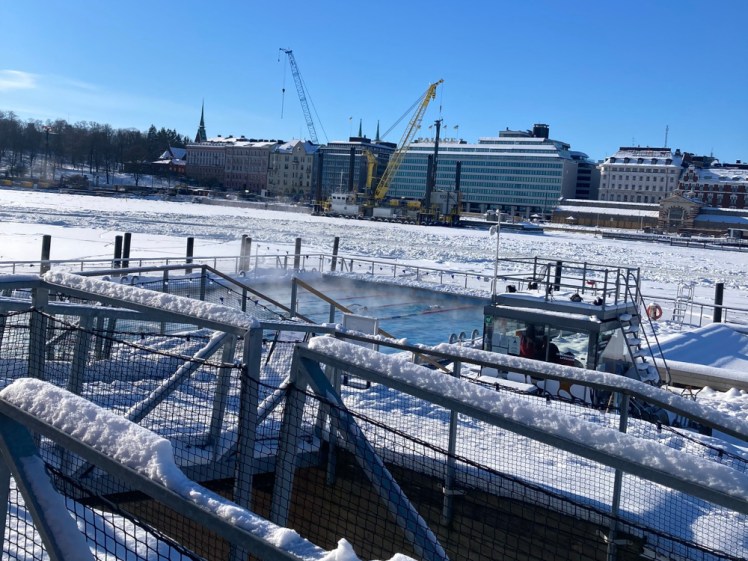 Allas Sea Pool in the snow. The pool itself is liquid and steaming gently but the decking and the harbour are both utterly frozen.