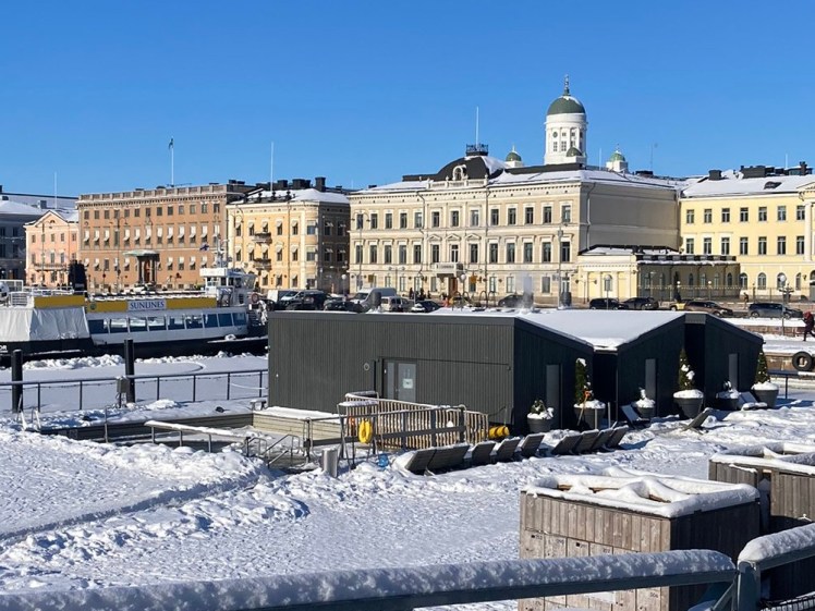 The sea pool, which you can just make out is pretty frozen. Next to it are three huts in dark wood with snow-covered roofs.