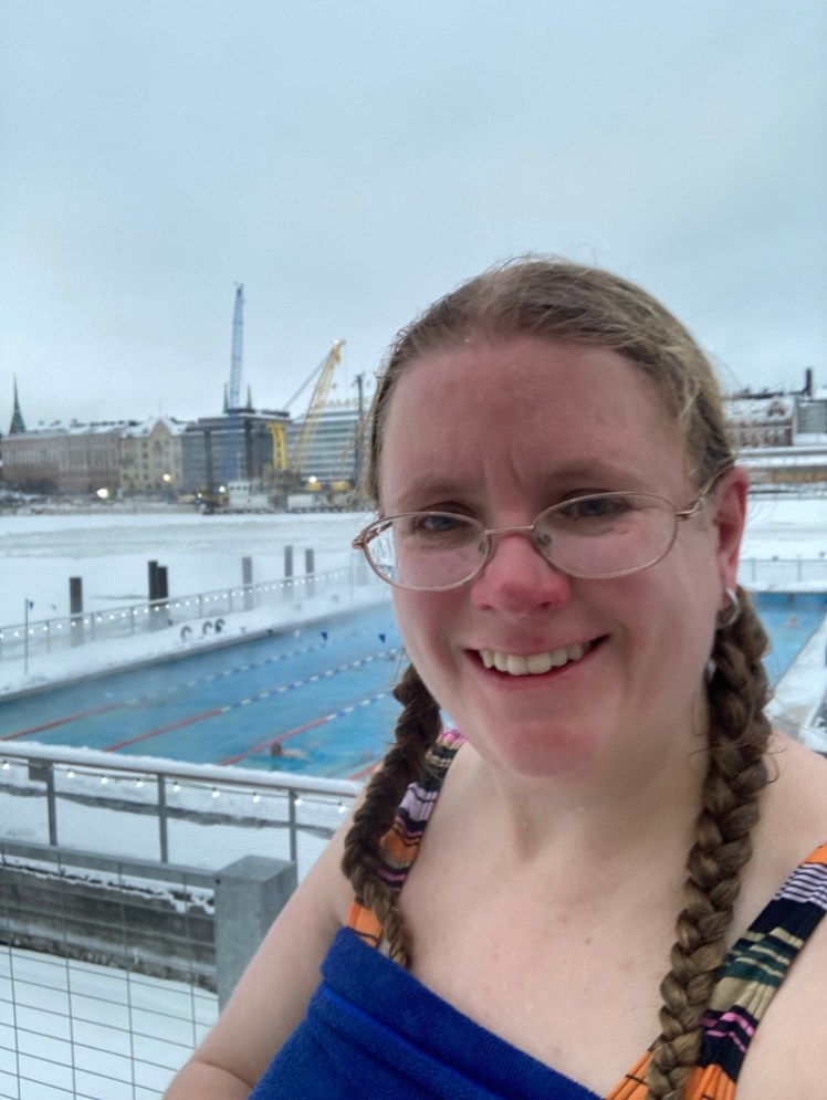 A selfie in swimsuit and towel, looking a bit frozen (although I'm actually pretty fresh from the sauna) in front of the pool, out in the snow.