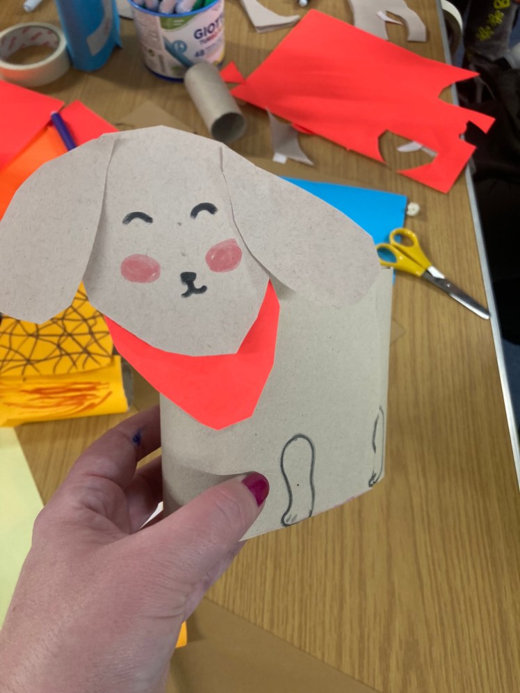 A penholder made by a Brownie. It's two toilet roll tubes stuck together and then covered with a piece of grey paper decorated to look like a really cute dog with a neon orange bandana.